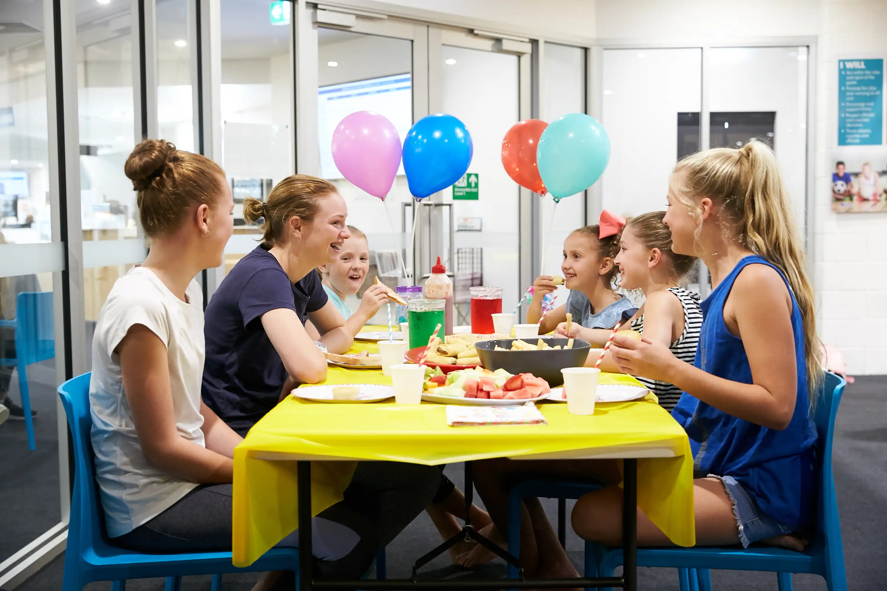 Young people at birthday party with balloons and food.