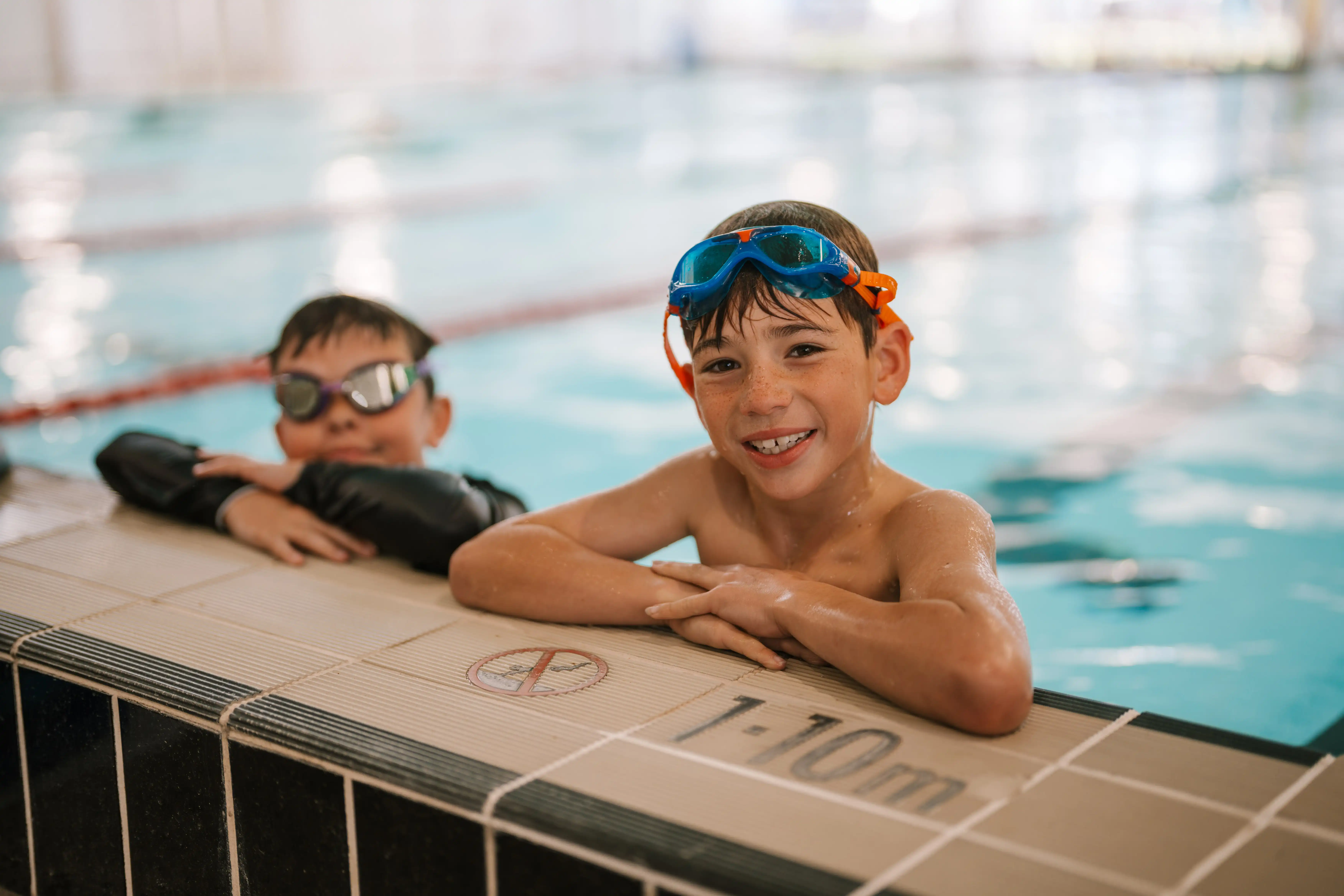 Two children leaning on side of pool edge.